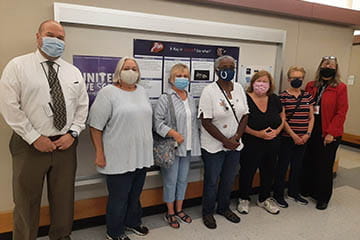 Seven individuals posing for a group photo in front of a poster board