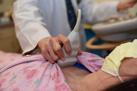 a doctor's hand holds an ultrasound machine over a patient's heart