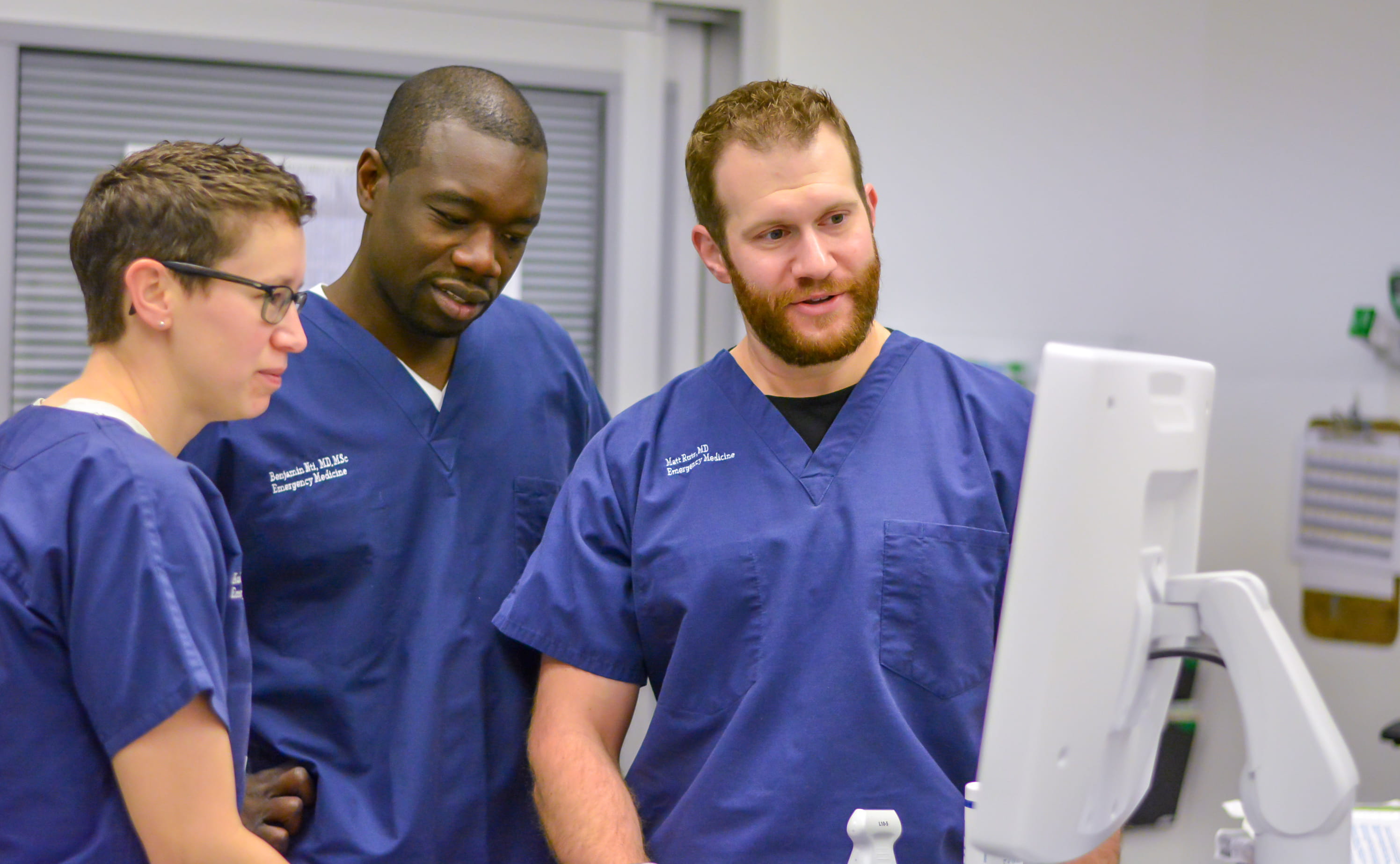 Three fellows wearing blue looking at a computer screen