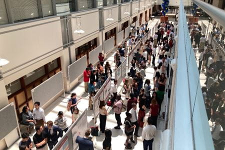 Students and others gather in an atrium to present research through posters.