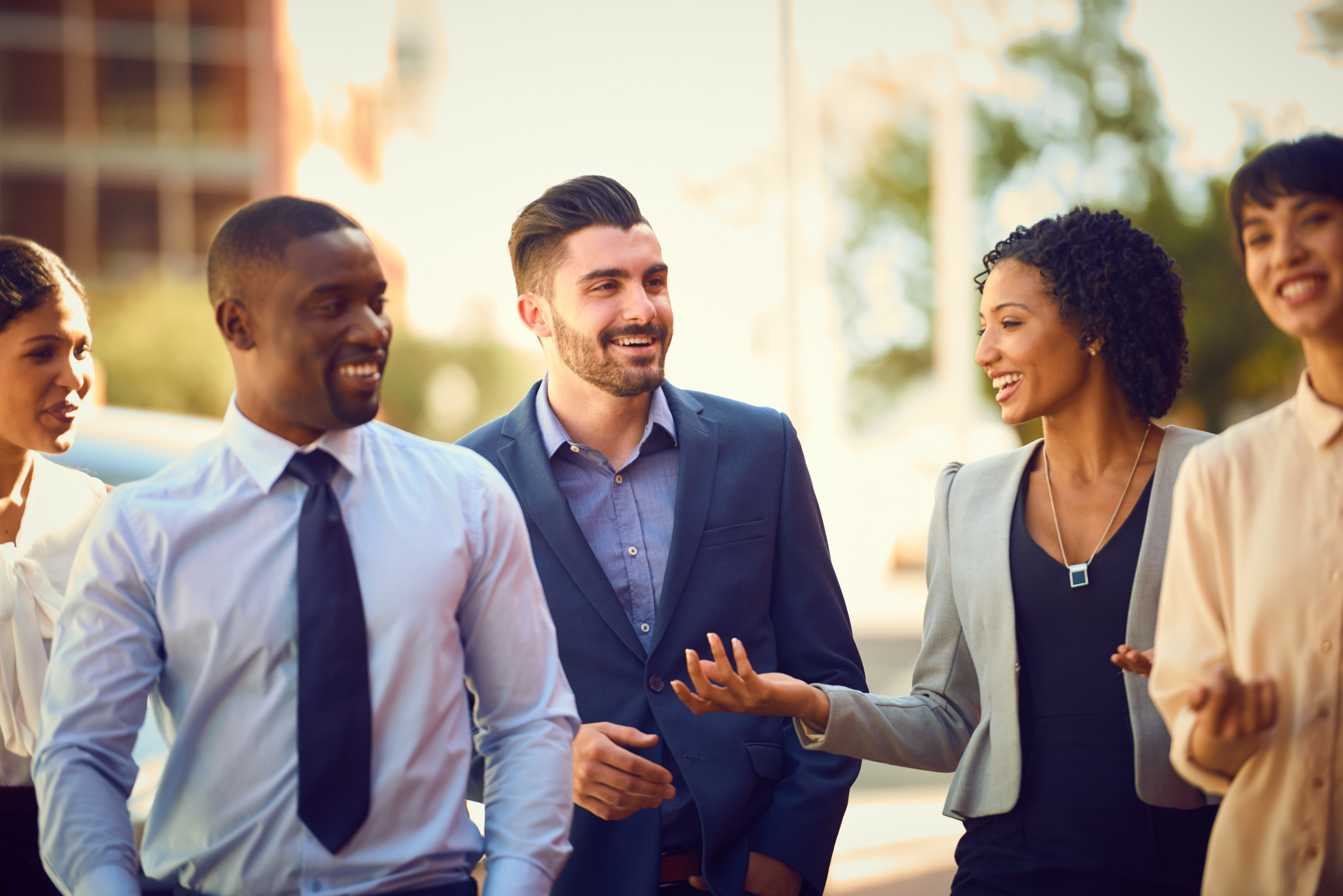 Five diverse young professionals walk outside.