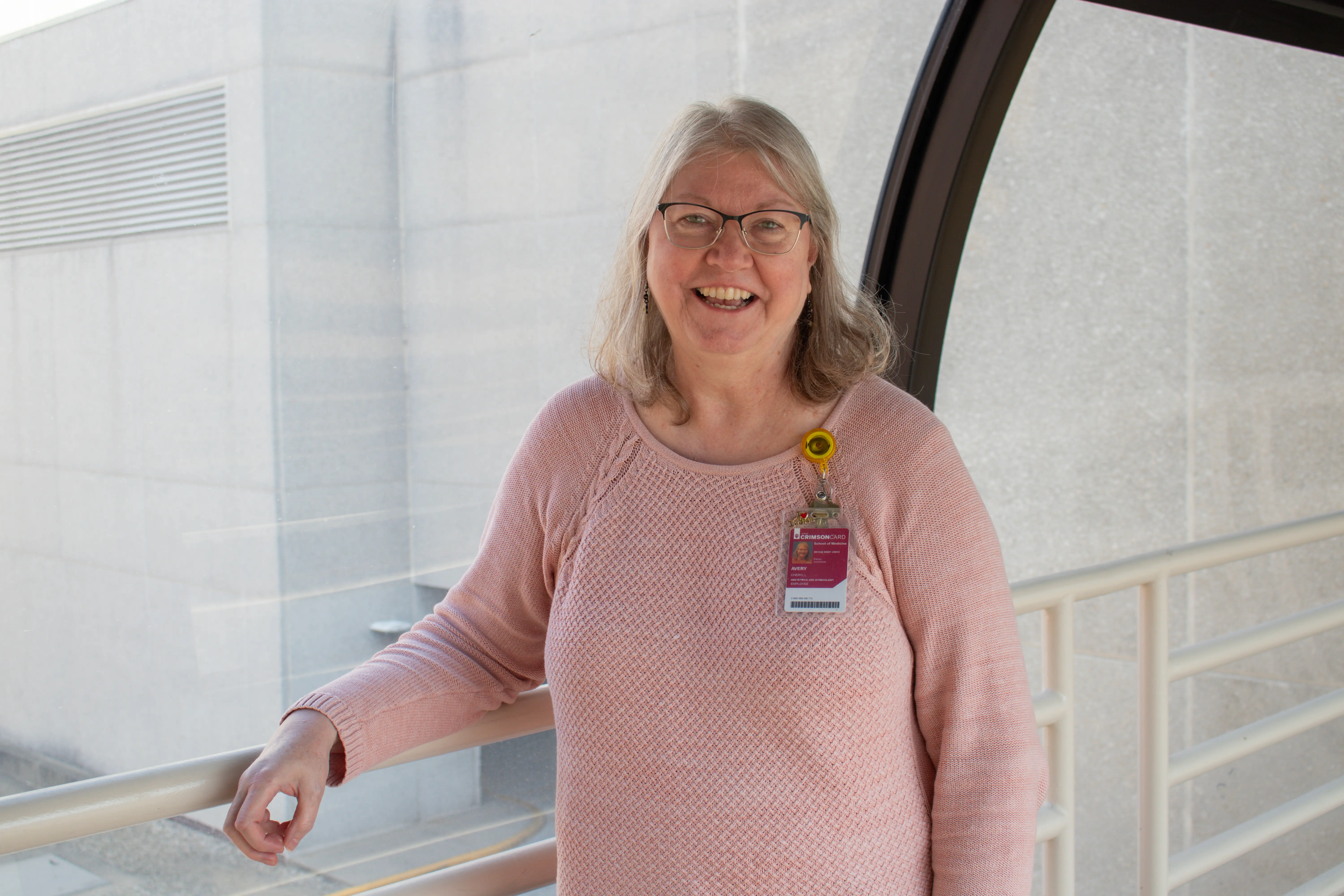 Cheryl Avery poses for her photo while leaning back against railing inside of a skywalk.