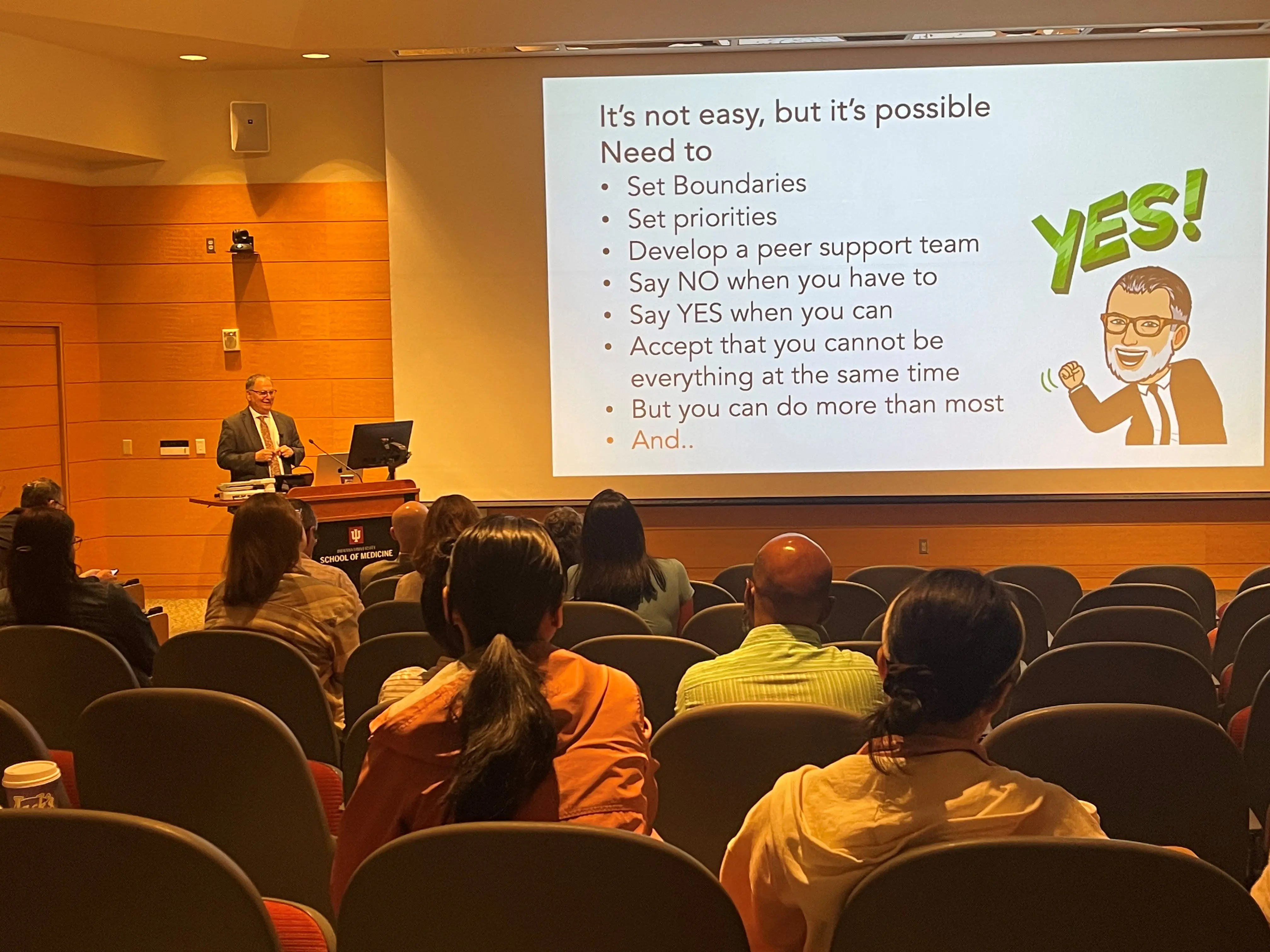 Naftali Kaminski, MD, speaks during Celebration of Science Day in May 2024. He is standing at a podium in front of a slideshow display and a small audience.