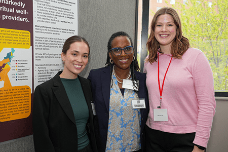 Three people pose for a photograph in front of research board at Ed Day 2024.