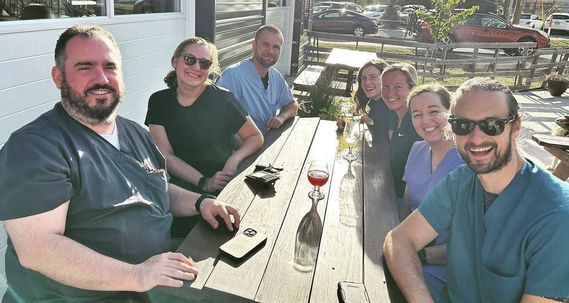 a group of fellows sit outside at a picnic table on a sunny day