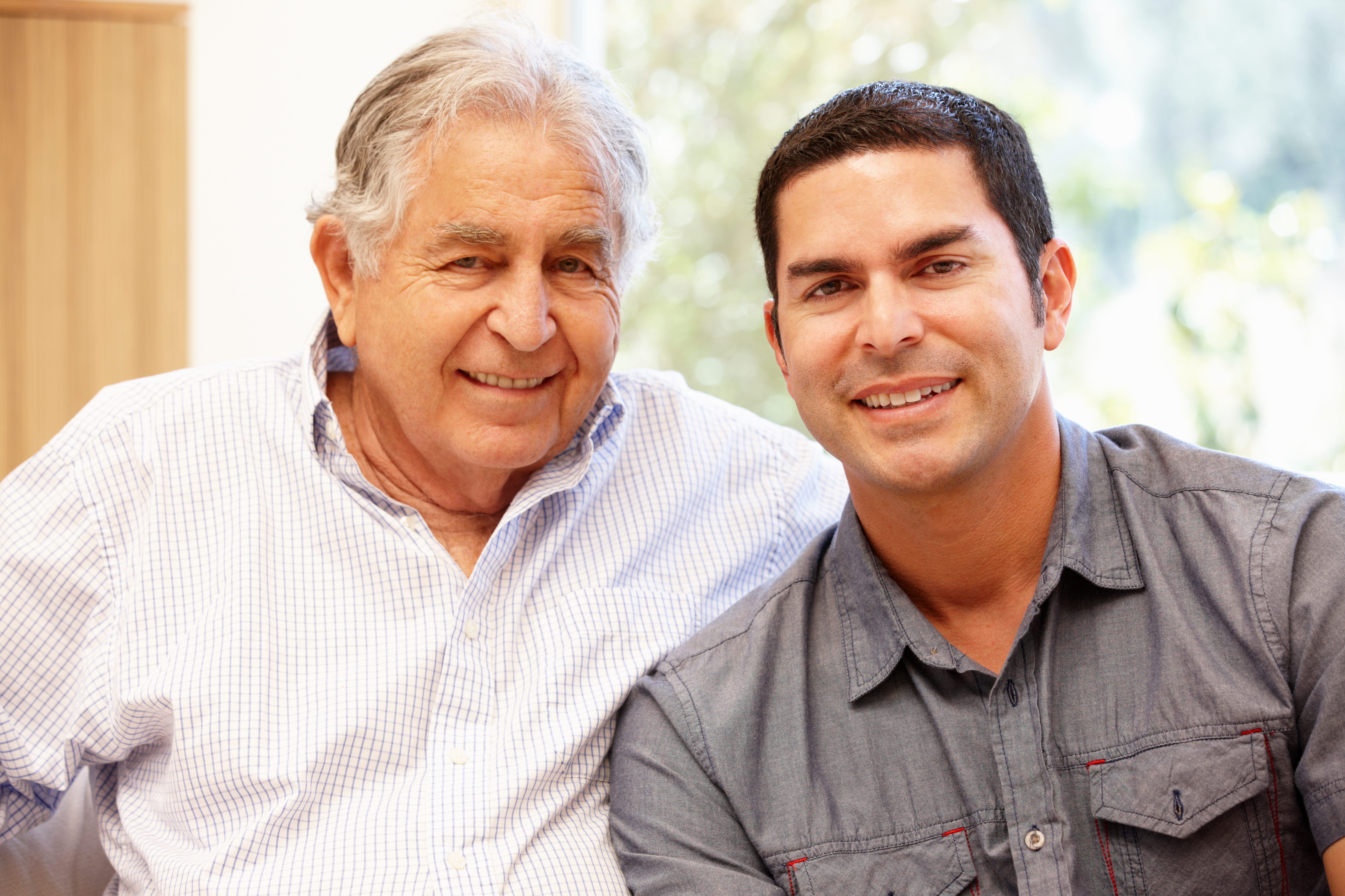 Hispanic father and adult son sitting side-by-side.
