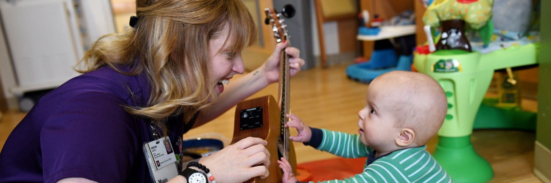 Music therapist Caitlin Krater smiles at a small child who is reaching up toward her guitar