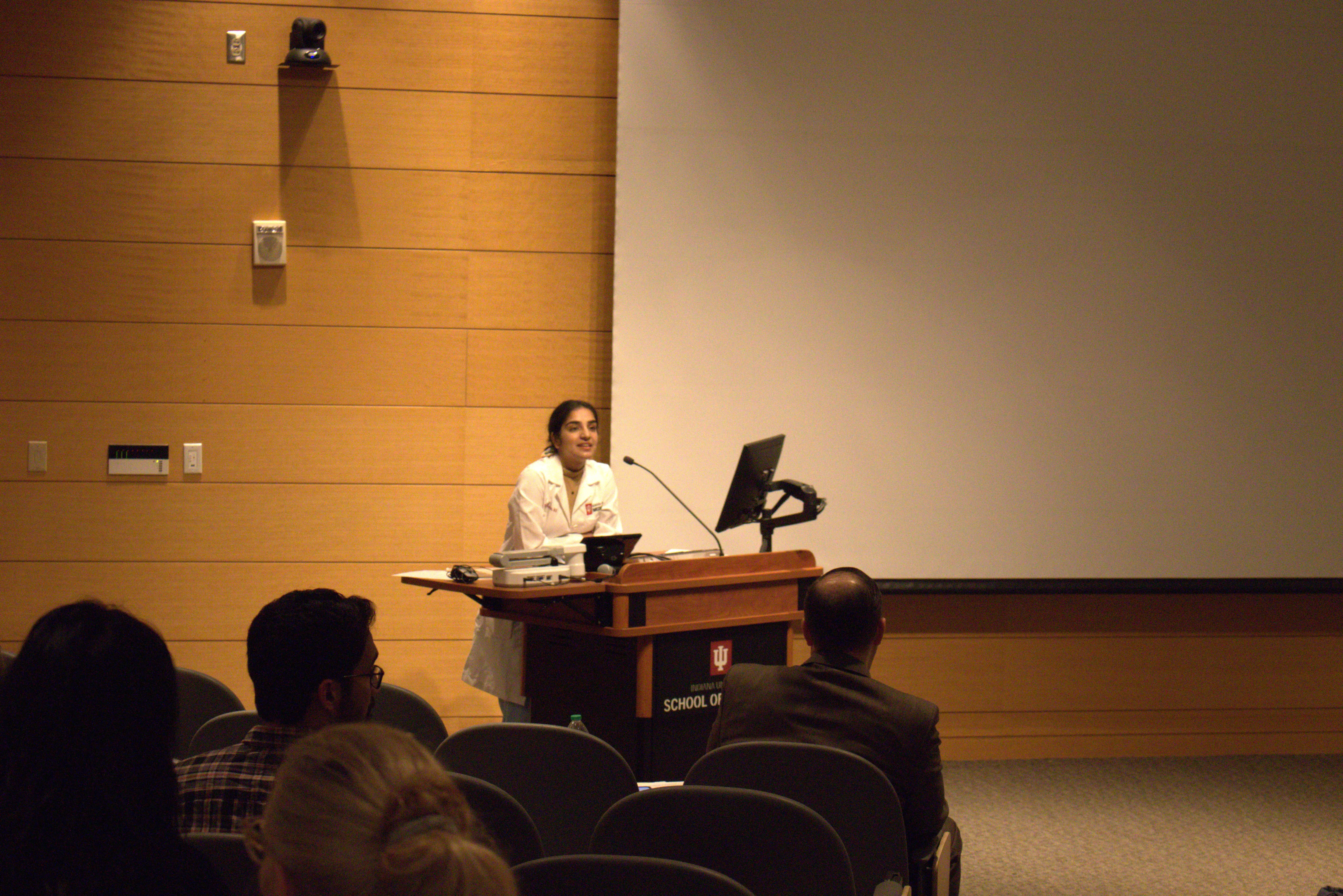 Dr. Komal Kumar stands at the lectern in front of the audience