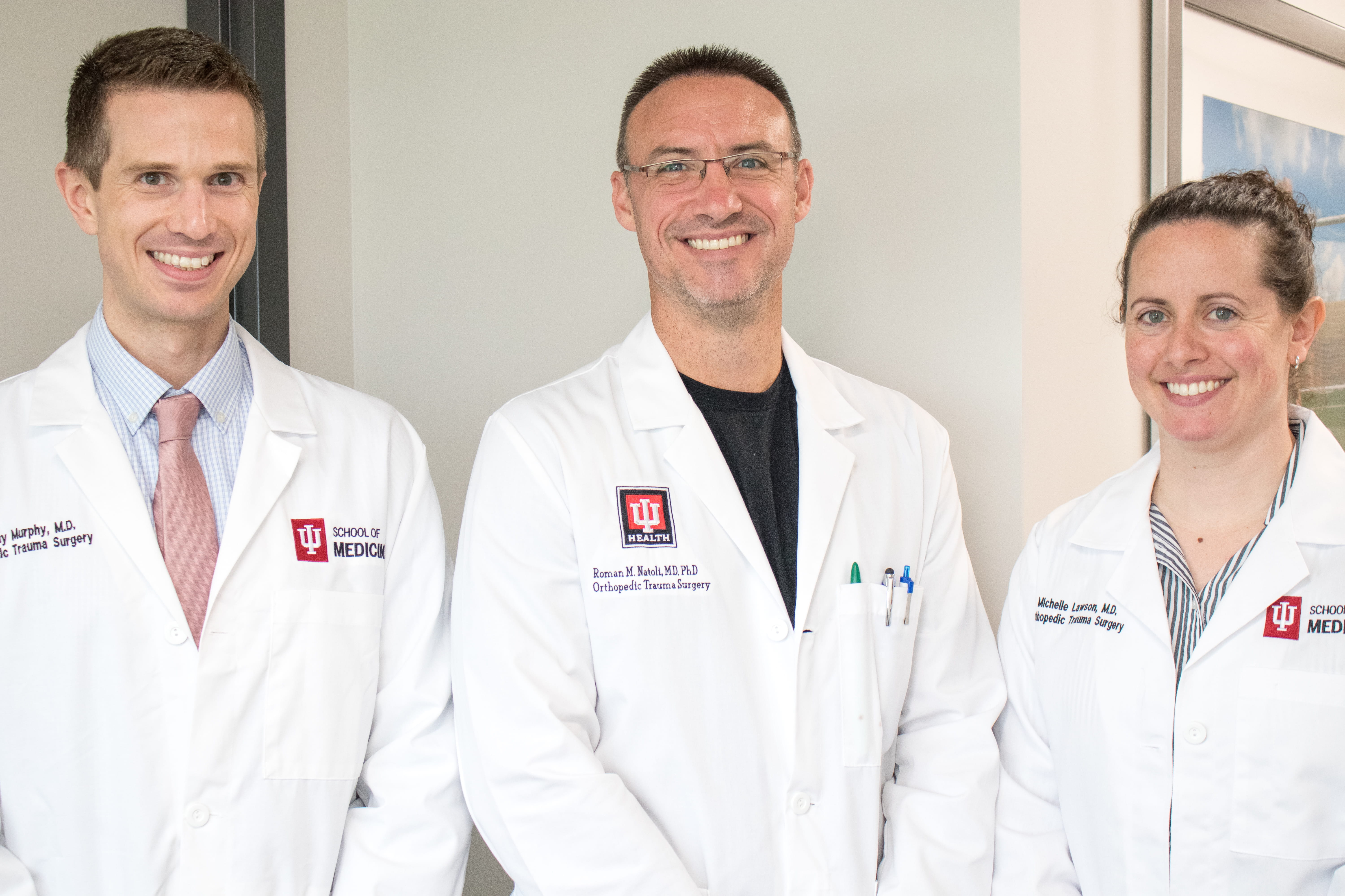 Two orthopaedic trauma fellows stand beside Roman Natoli, fellowship director. All 3 wear their white coats.