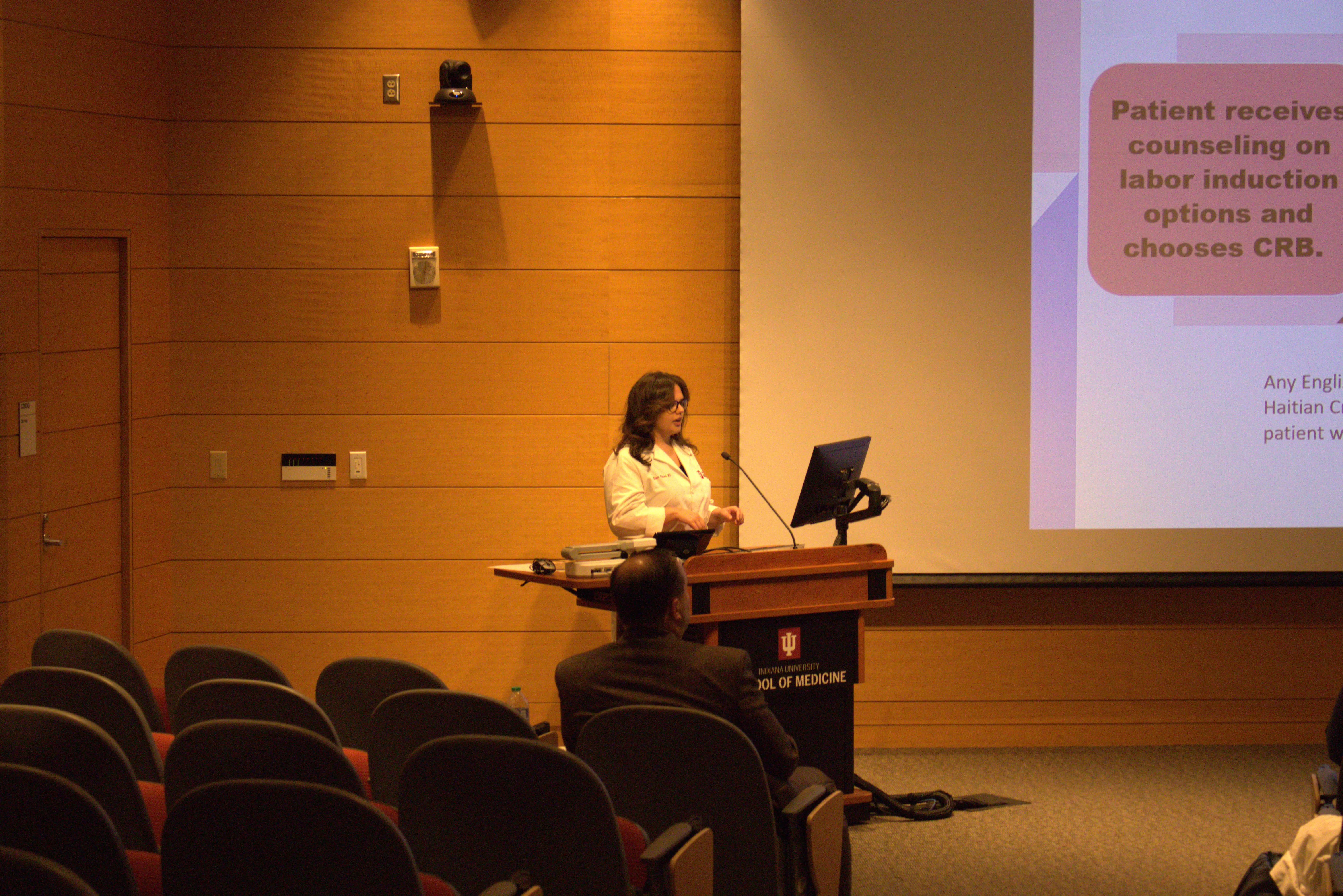 Dr. Allison Polidori stands at the lectern facing the audience in the auditorium