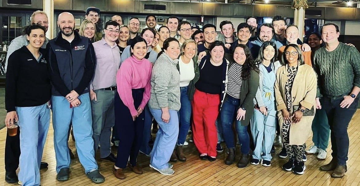 a large group of about 30 trainees and faculty stand together and smile