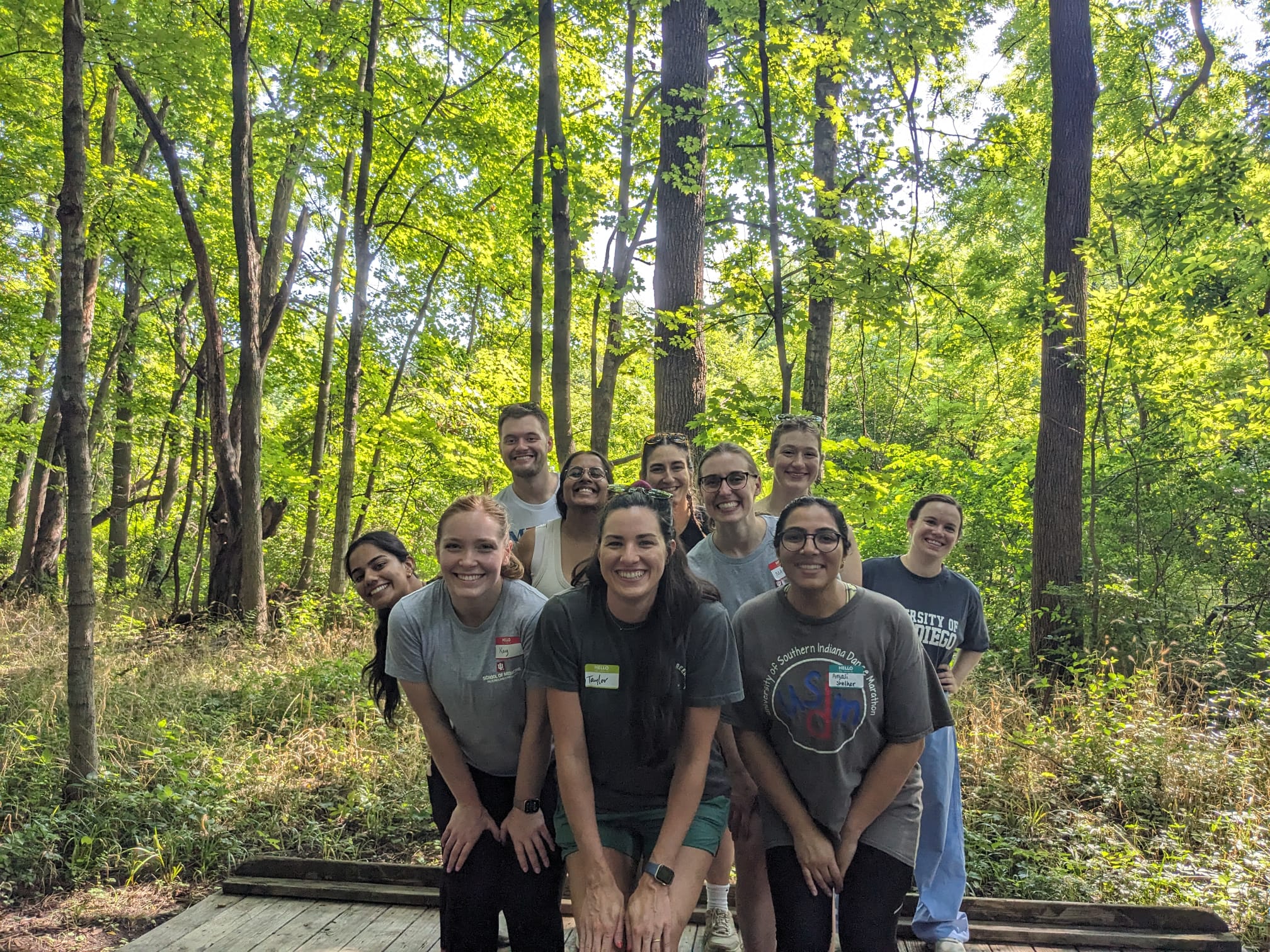 Residents stand crouched in two lines for their photo, with trees and nature behind them.
