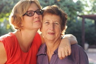 Older woman with auburn hair outside with her adult daughter.