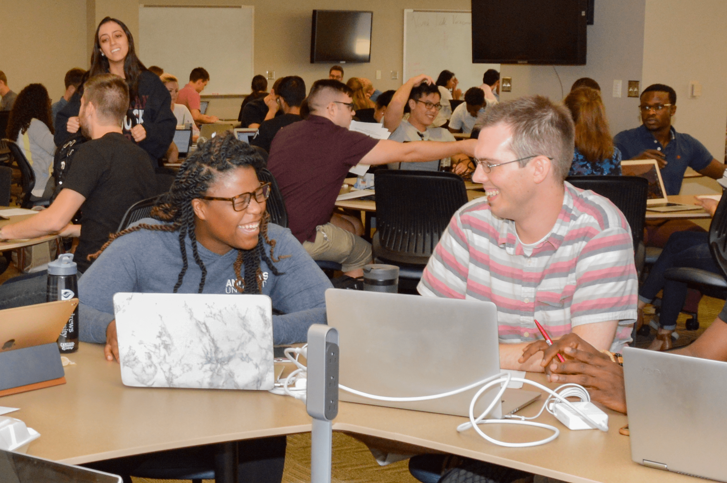 Two students with laptops sitting at a desk having a joyful conversation in class