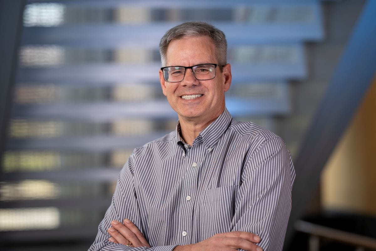 Man with folded arms poses in front of staircase. 