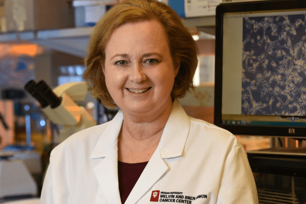 A headshot of Karen E Pollok, a woman with mid-length hair smiling and wearing a white IU labcoat.