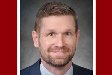 A headshot of John Leck, a man with short brown hair and a beard