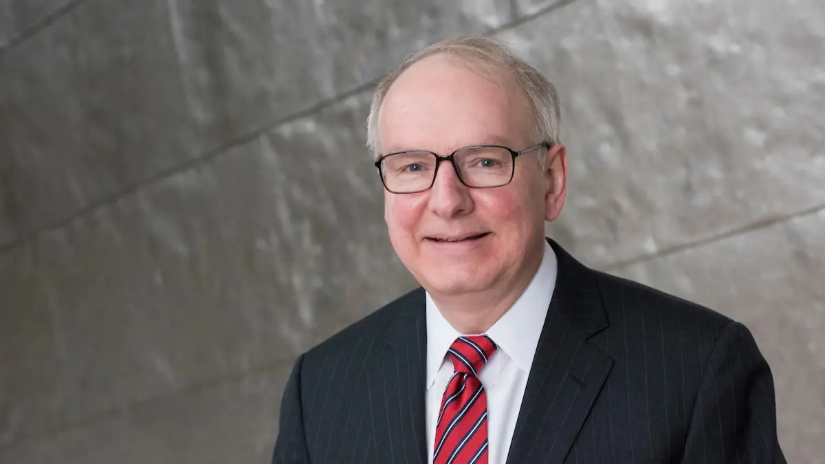 Dean Jay Hess wearing a dark suit, red tie and glasses.