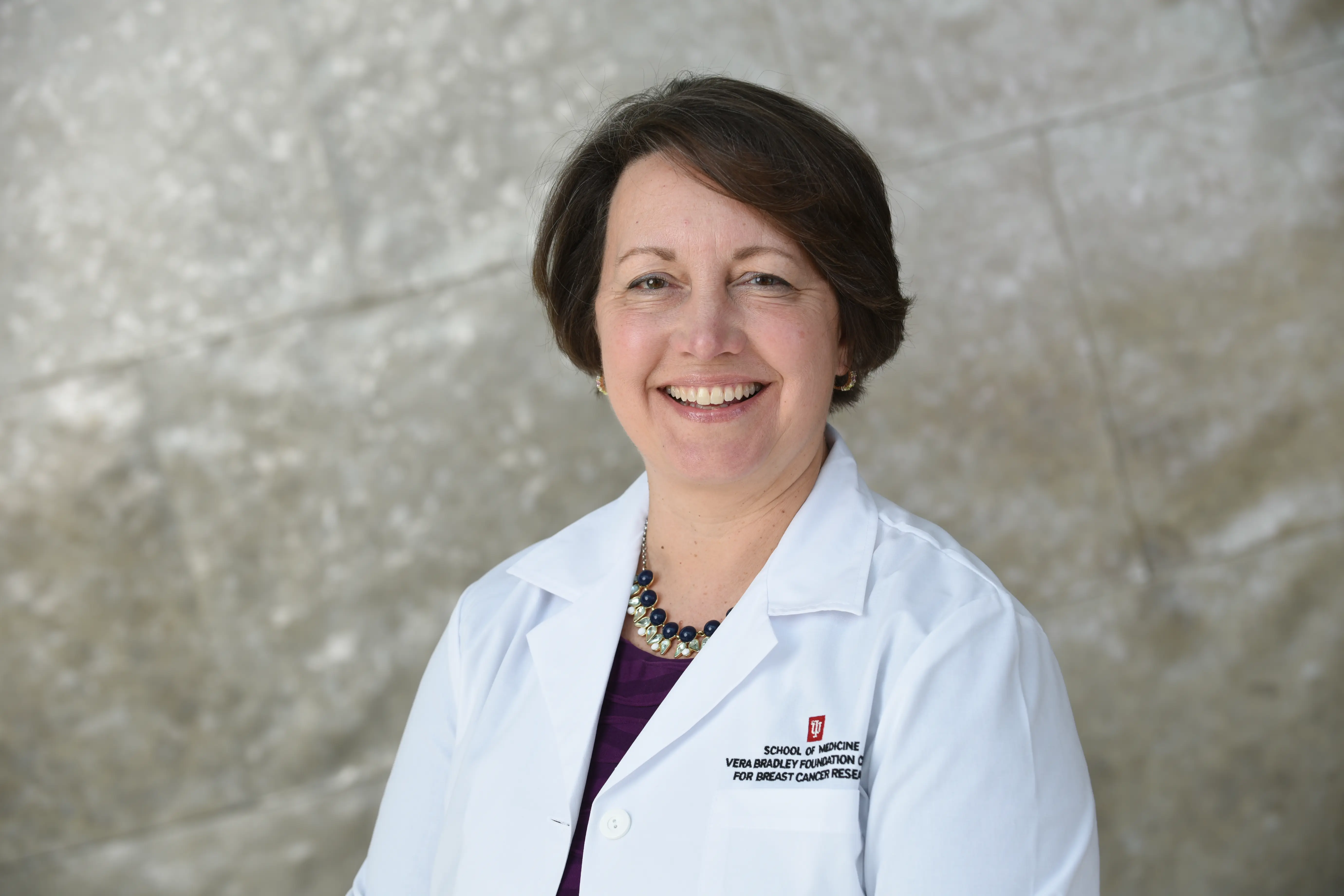 Kathy Miller smiling in a lab coat in front of a silver wall.