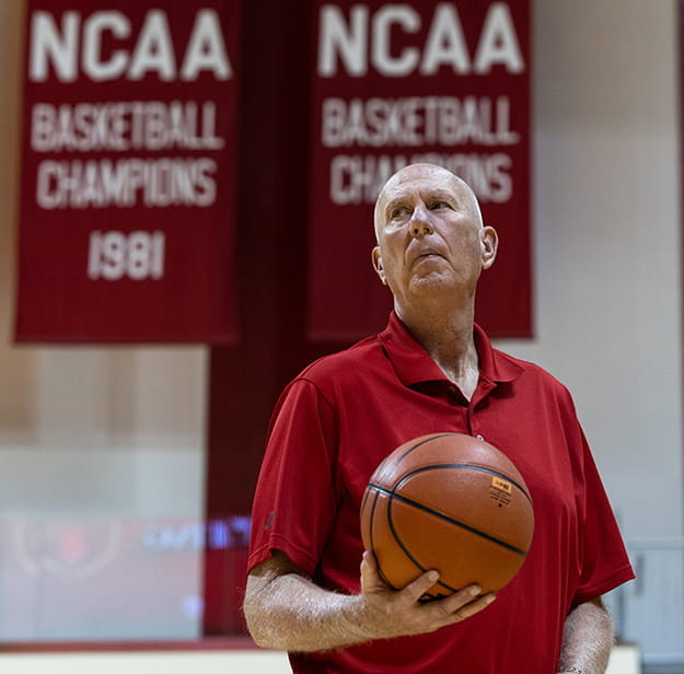 Ted Kitchel holds a basketball. Behind him are NCAA basketball champion banners that hang in Assembly Hall.