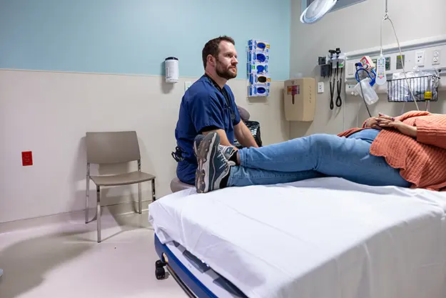 Matt Rutz sits at the bedside of a patient in the emergency department.