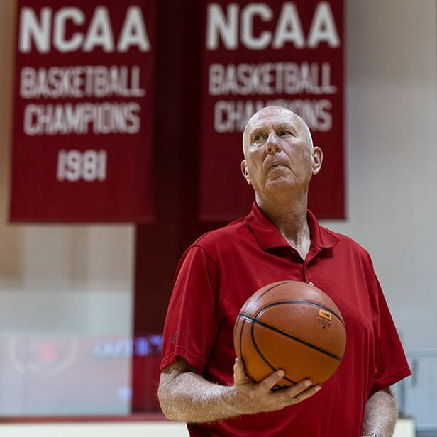 ted kitchel holds a basketball in assembly hall in front of the school's championship banners