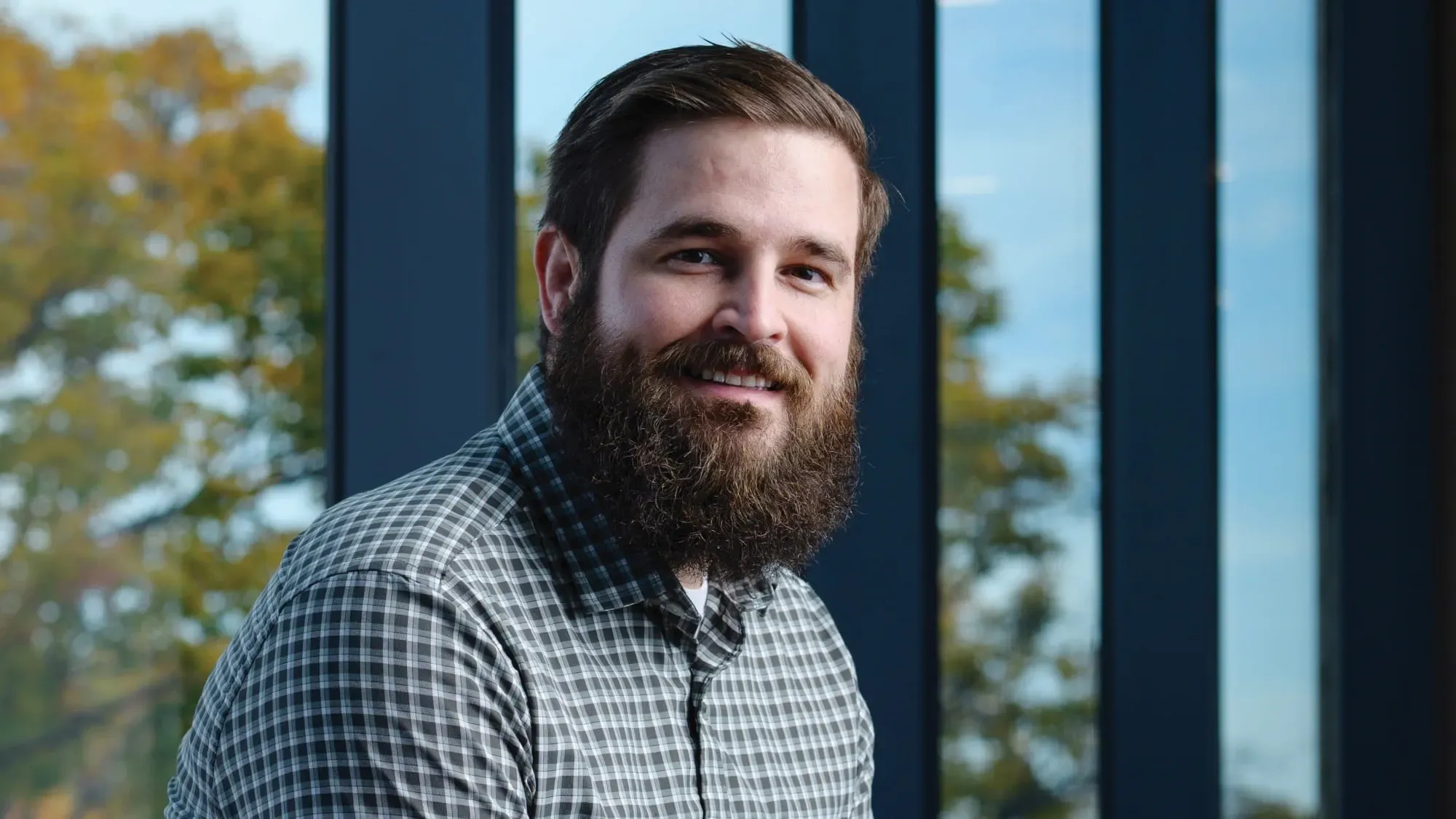 Travis Johnson, with short dark hair and a beard, sits outside on a bright sunny day