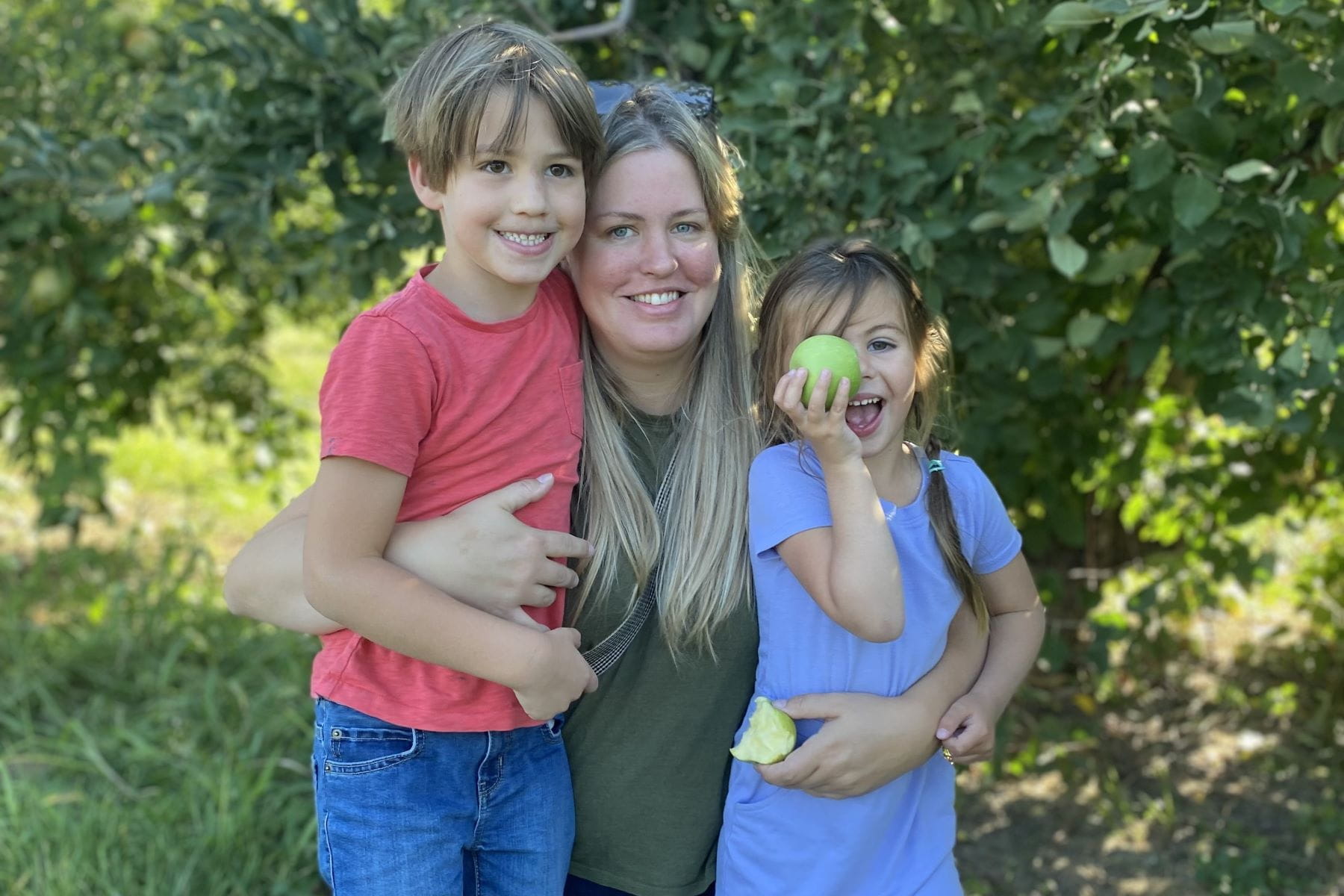 emily wachner with her two kids in an apple orchard on a sunny day