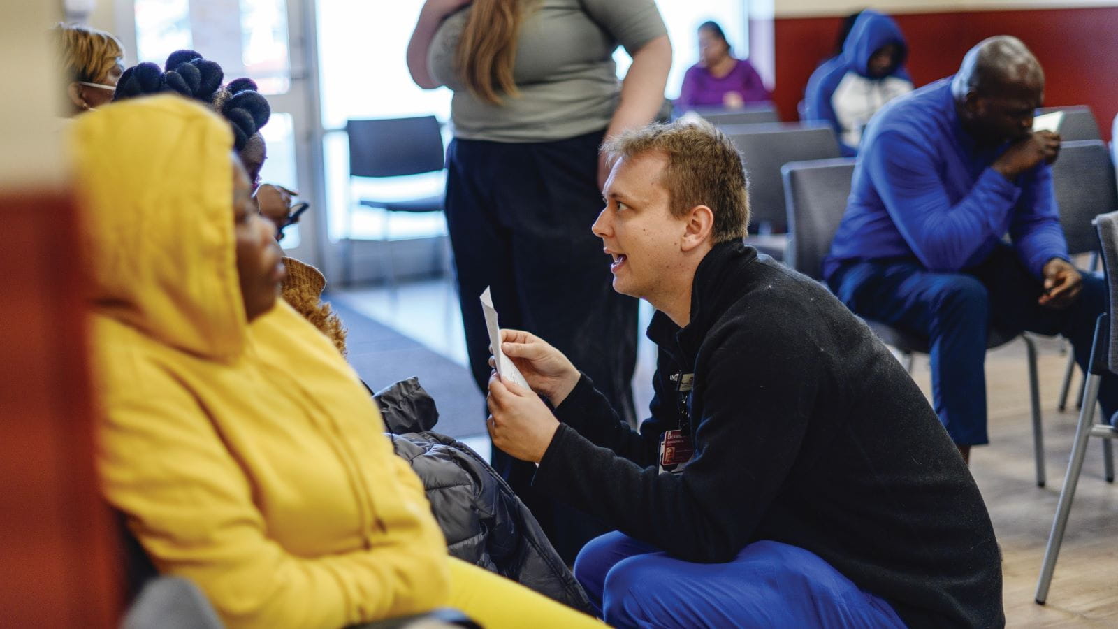 A medical student crouches down to talk at eye level with a seated patient at the student outreach clinic in Indianapolis.