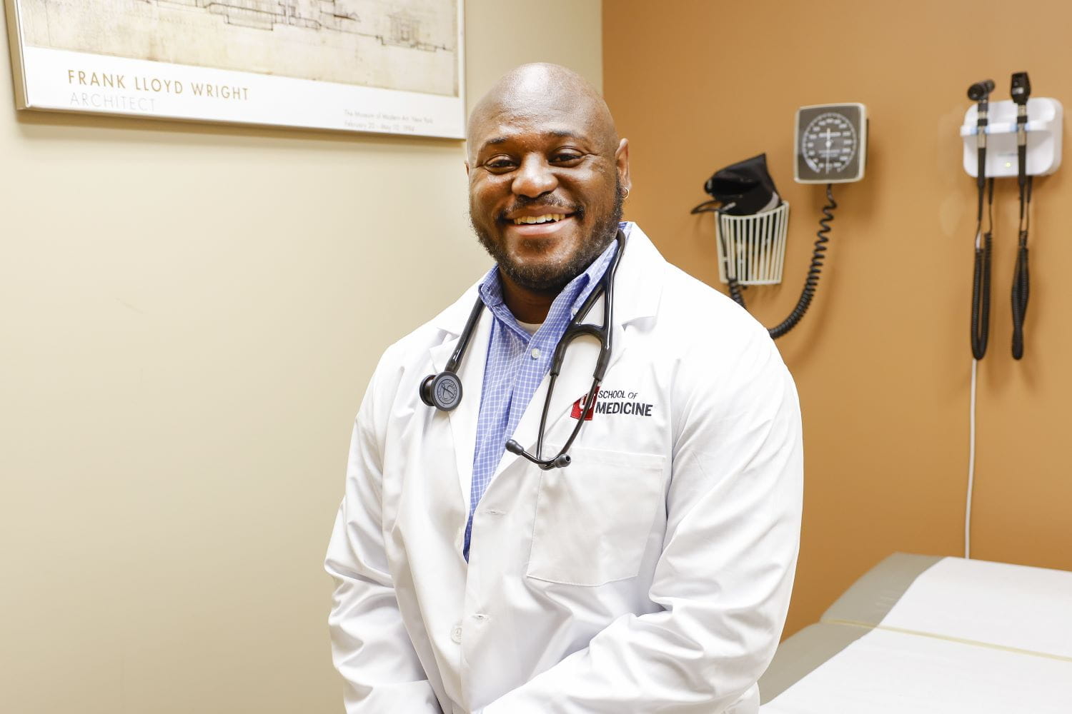 Mason Gionte, wearing a white coat and stethoscope, sits in an exam room