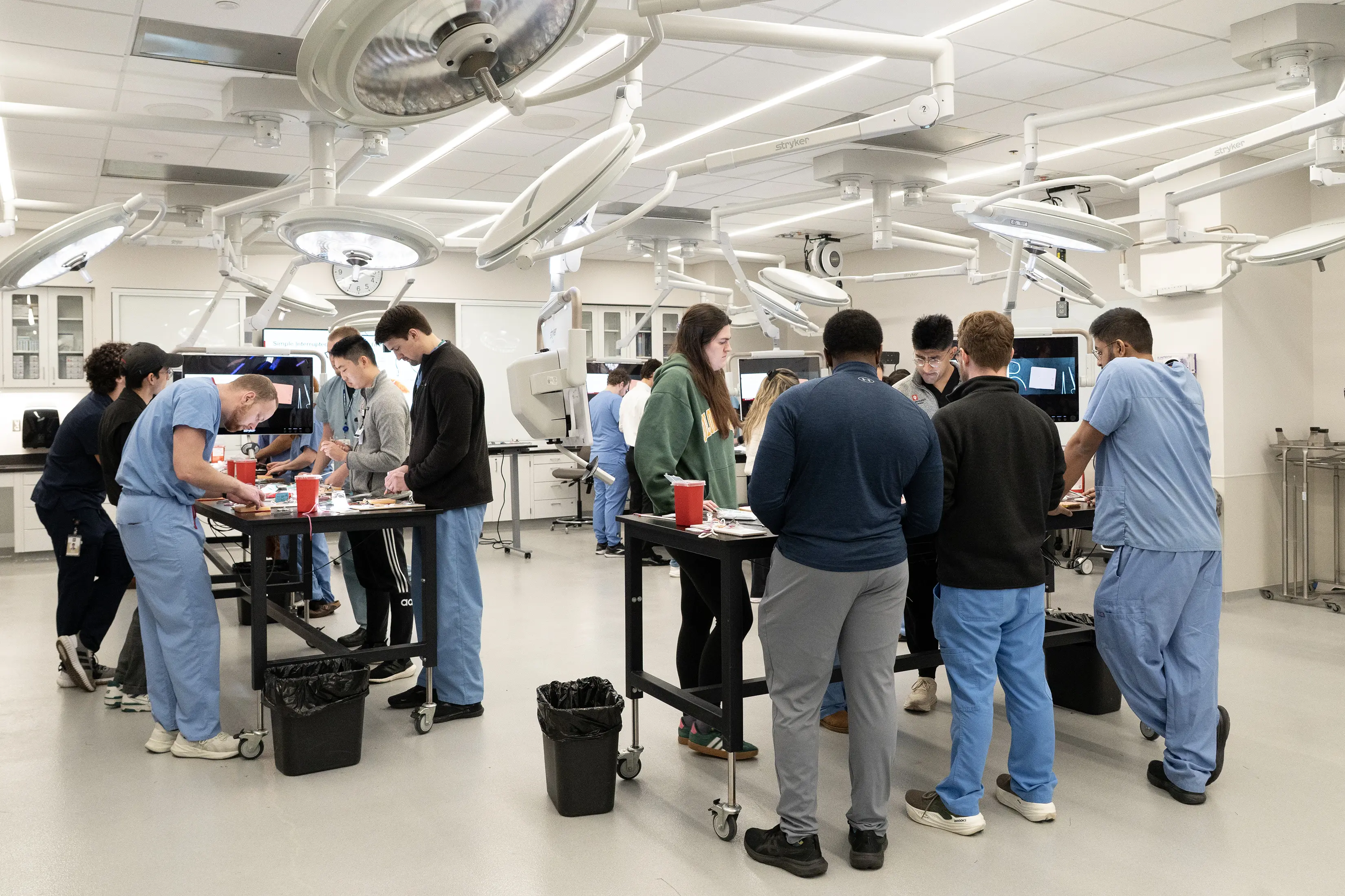 A dozen trainees work at standing tables in the surgical skills lab