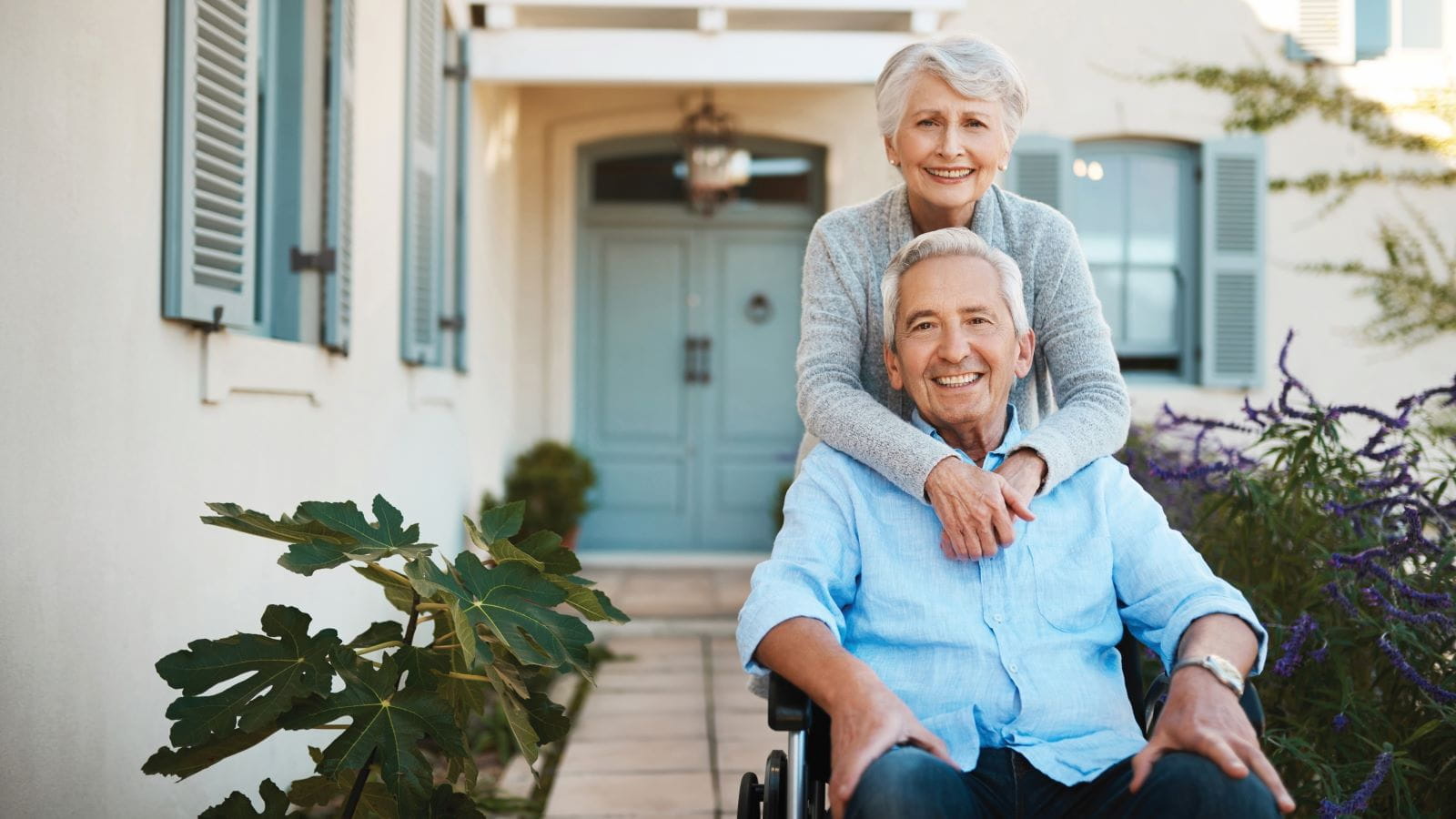 Cheerful senior man in a wheelchair relaxing with his wife in their backyard at home.