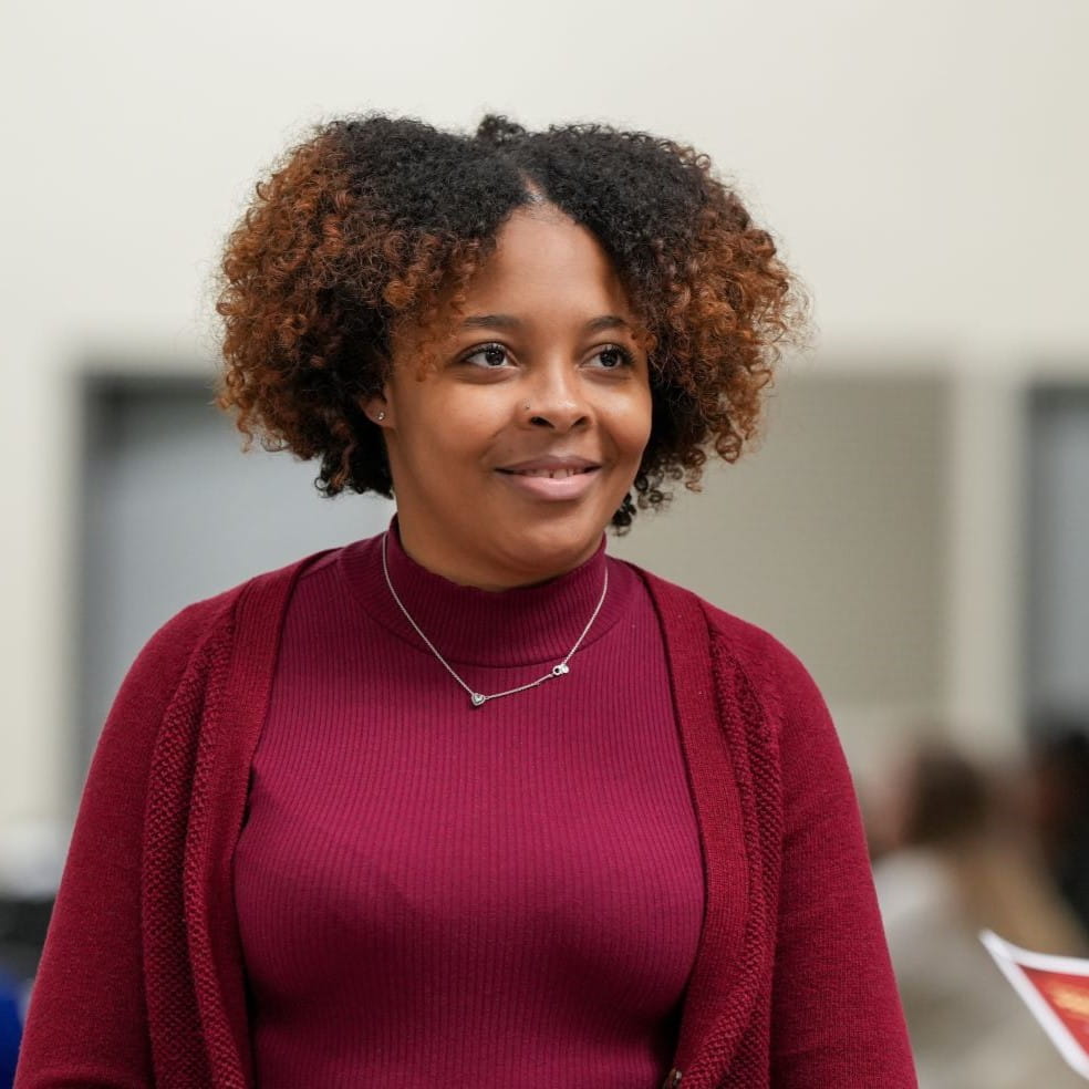 a woman with dark curly hair and a maroon shirt and cardigan.