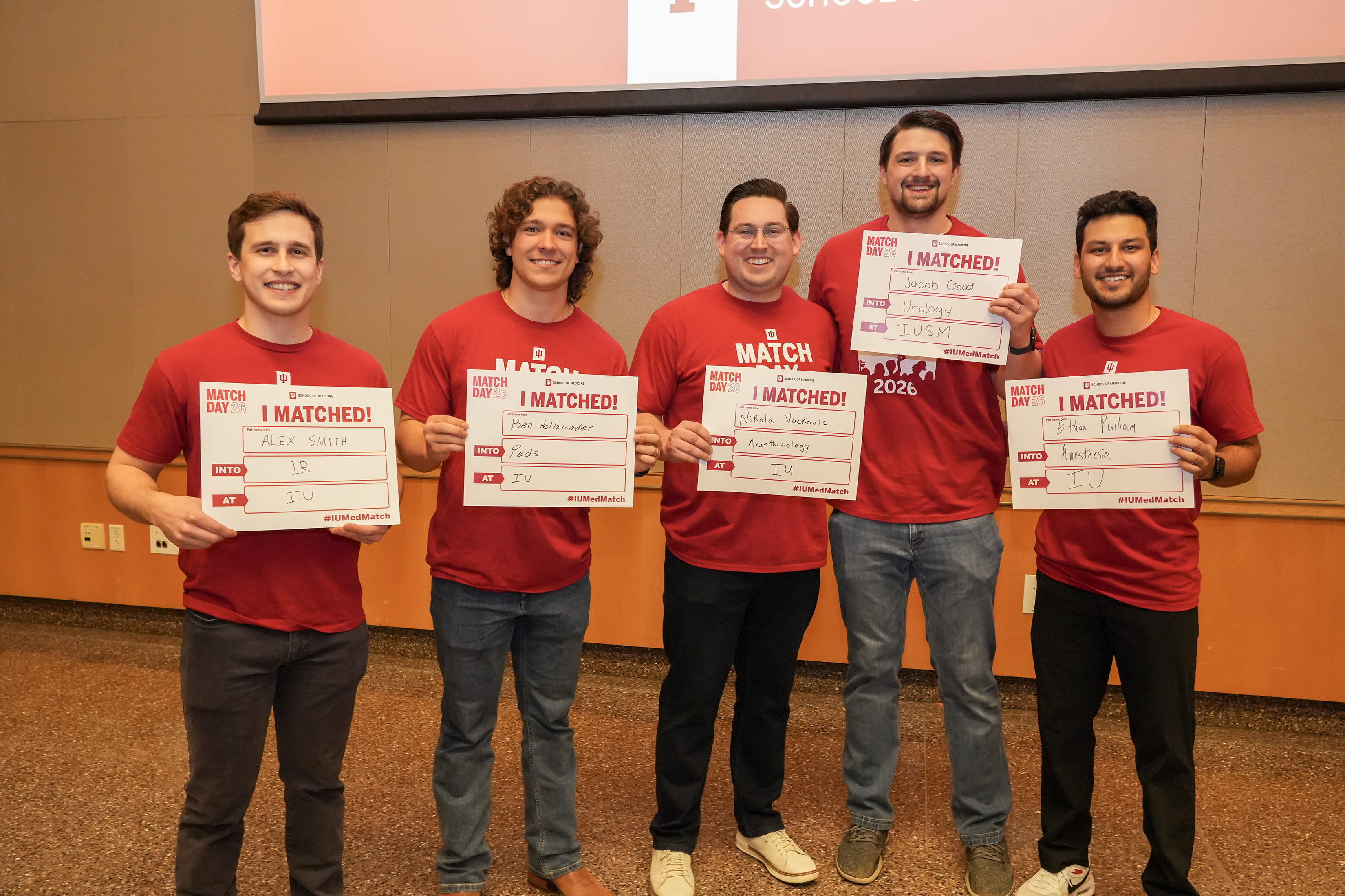 Five men in red shirts hold up matching signs. 