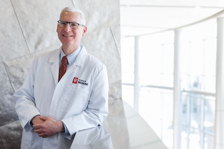 A man in a white lab coat poses on a stairwell.