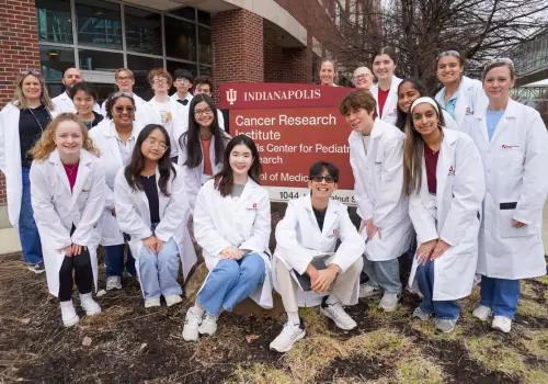 Group of MMIA students from 2026 the program posing in their white coats near the IU Indianapolis cancer center sign
