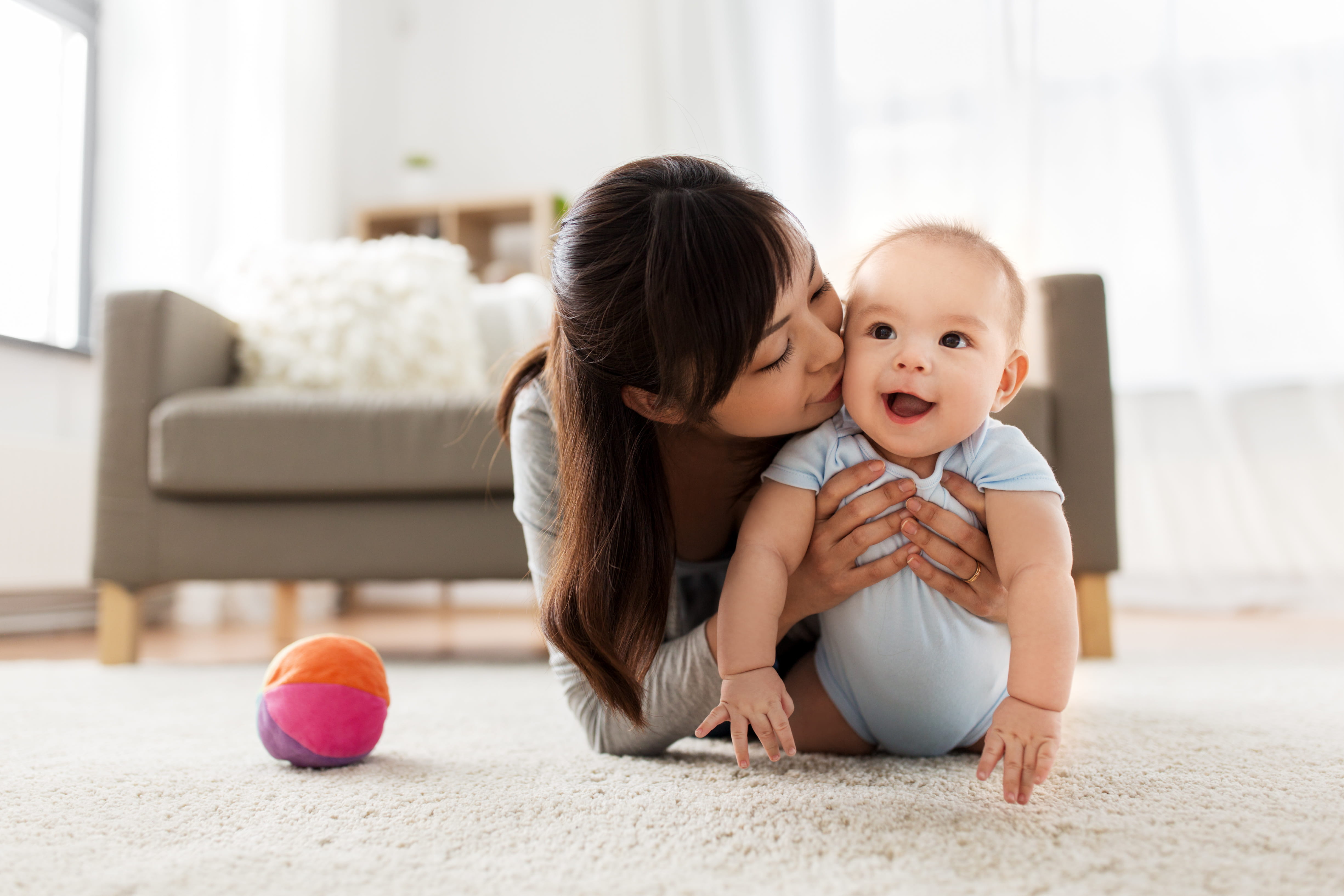 person crouched down on ground holding smiling baby in home