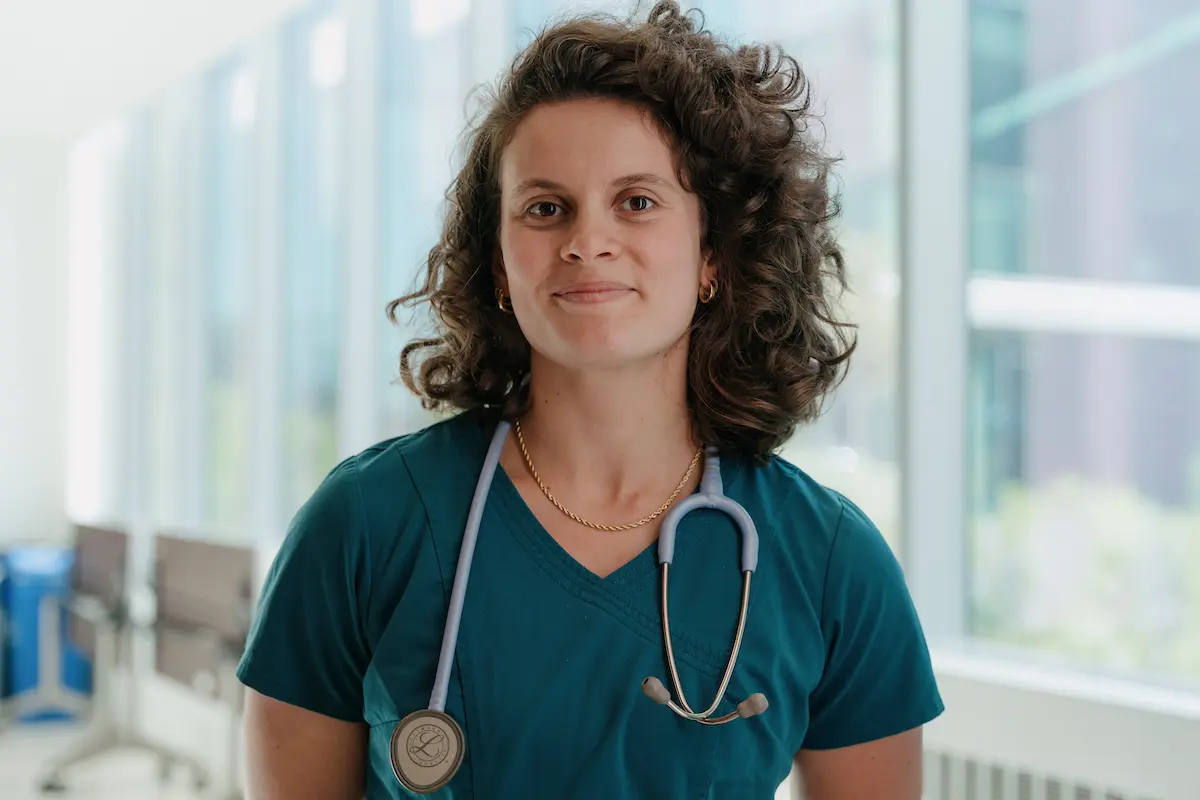 a student in blue scrubs with a stethoscope around her neck looks proudly at the camera
