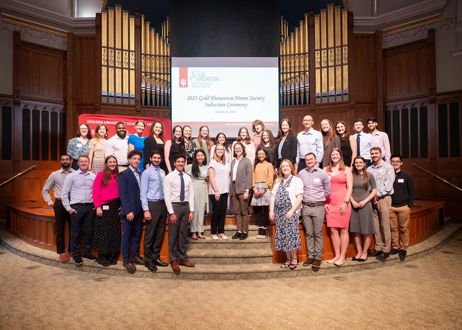 All the members of the 2025 Gold Humanism Honor Society standing on an elevated stage in a church. Behind them are the pipes of an organ.