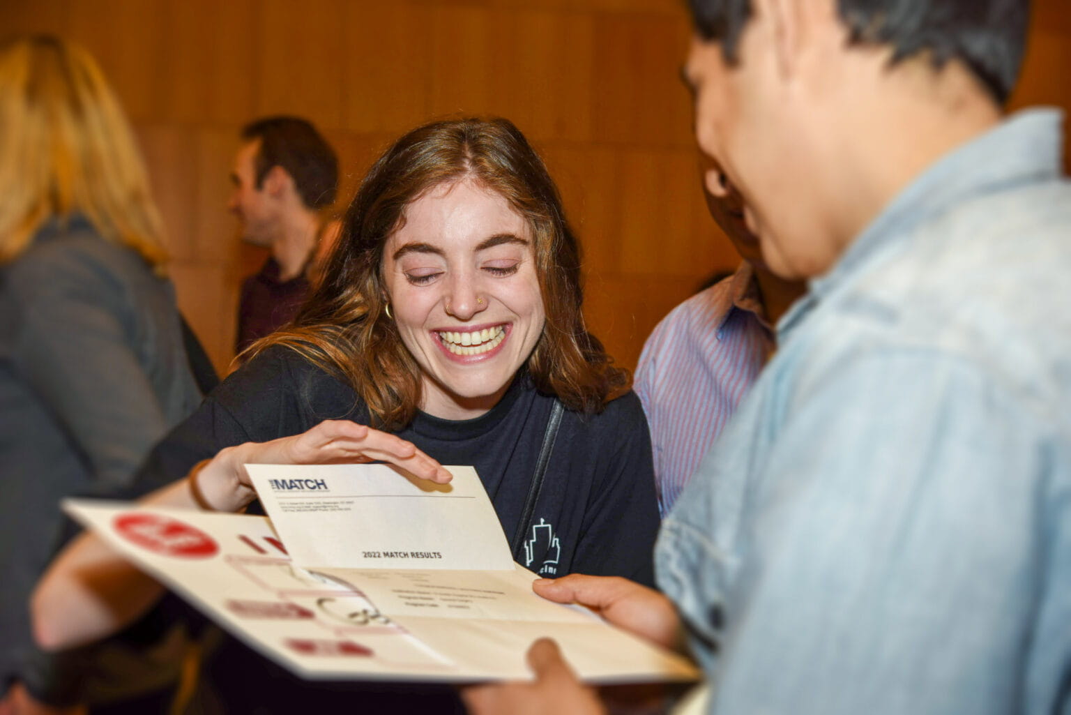a student has a huge smile on her face as she shows a friend her match letter