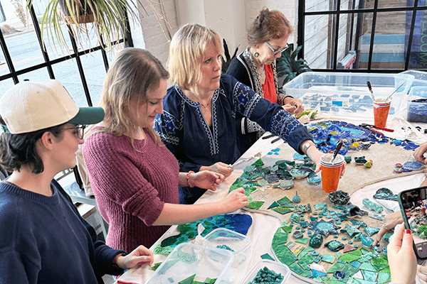 Joani Rothenberg (third to right) works with IU School of Medicine students in assembling a mosaic on the table in front of them.