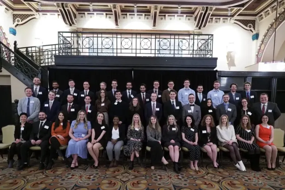 3 rows of sharply-dressed students with name tags, all smiling in a fancy event center
