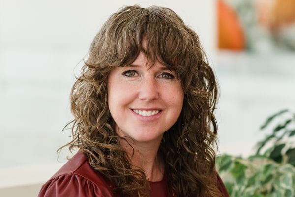 headshot of Brittany Needham against a white background with a green plant in the corner 