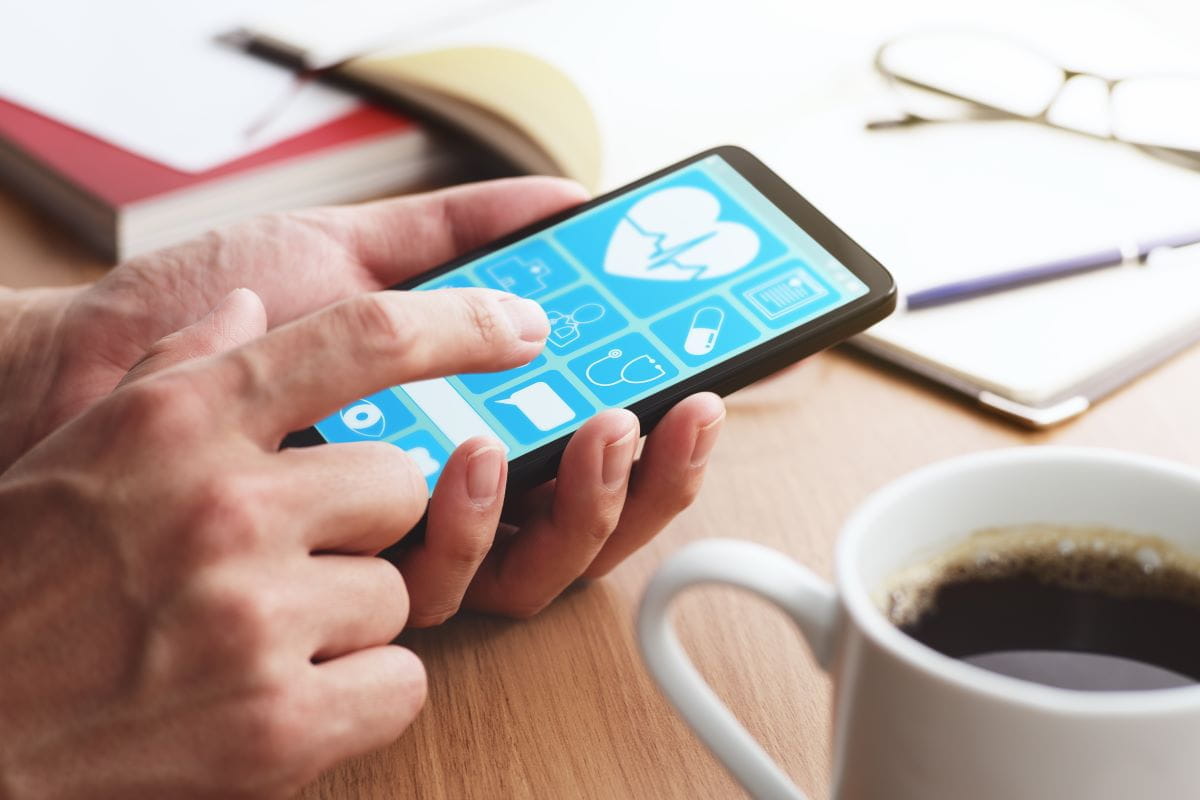 Closeup of male hands touching a phone screen at a table with coffee and a notebook