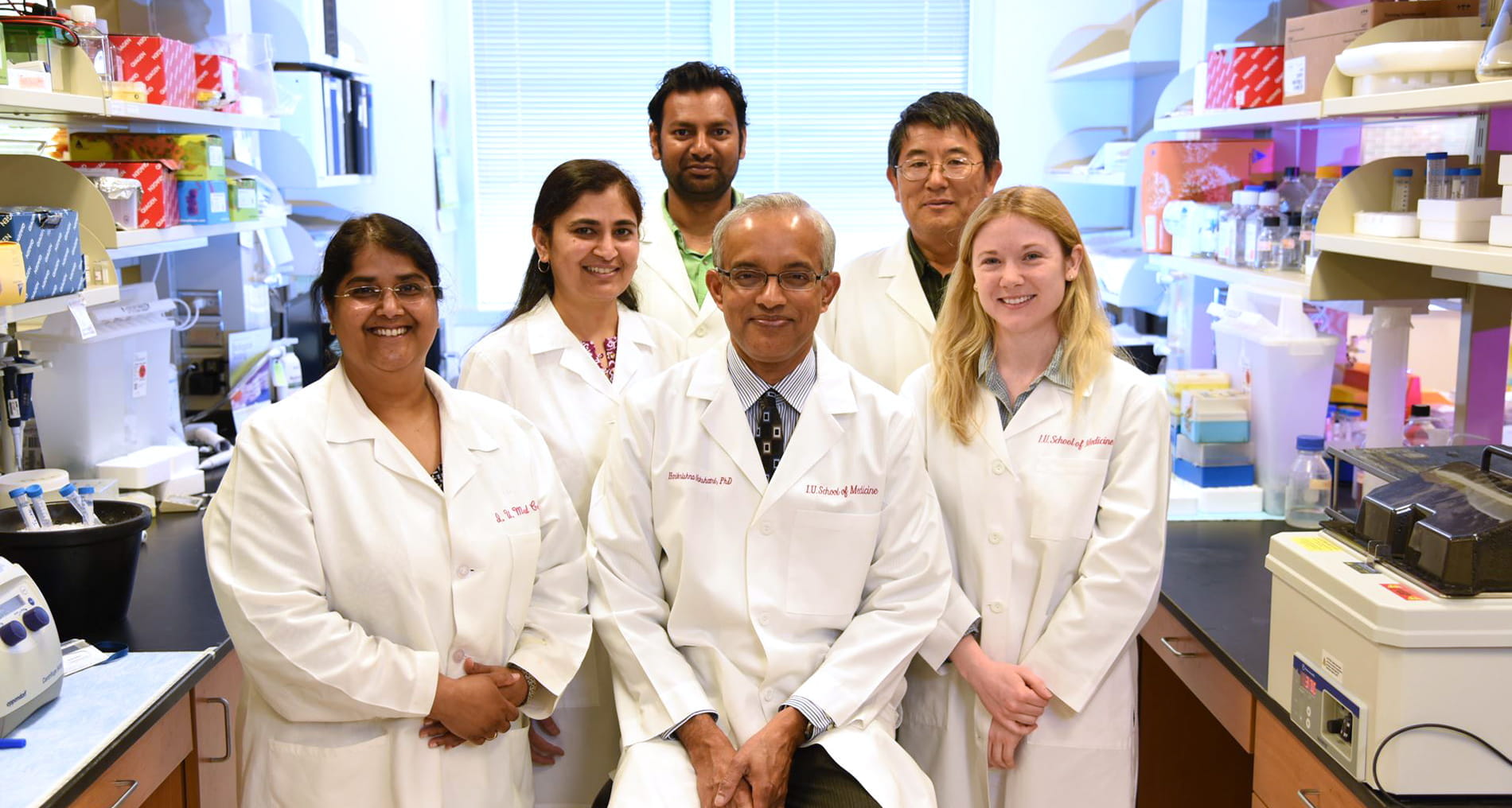 a team of researchers in white lab coats pose for a photo in their lab