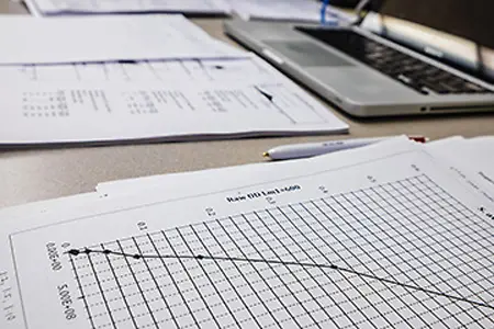 a paper with a graph on it sits in the foreground with a laptop in the background