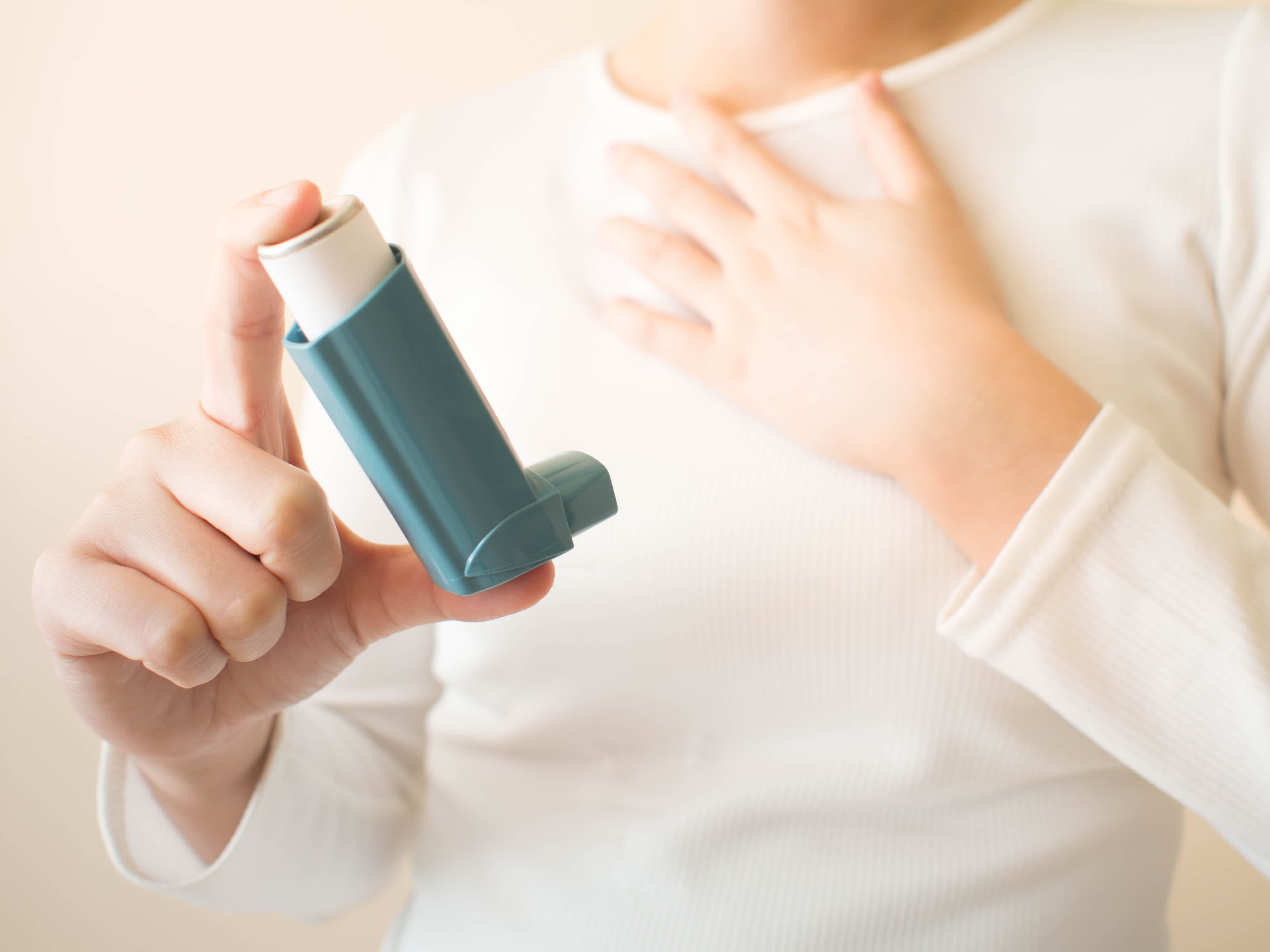 a person with their hand on their chest holds an inhaler