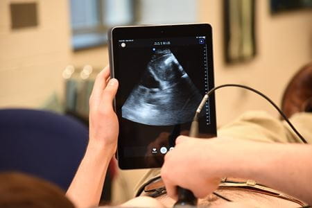 a close up photo shows hands holding a display screen and a POCUS wand against a patient's stomach