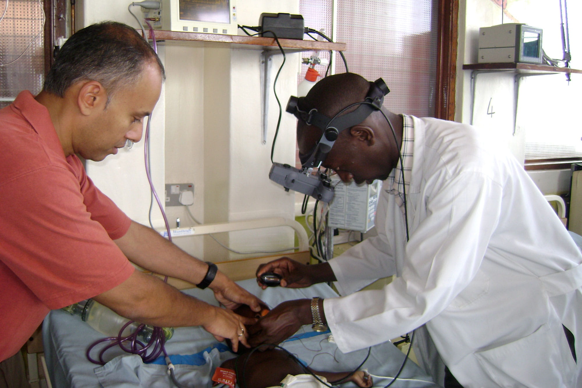 Chandy John helps a medical officer look at the retina of a child with malaria