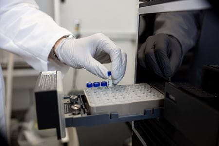 A researcher's gloved hand lifts a glass tube from a tray